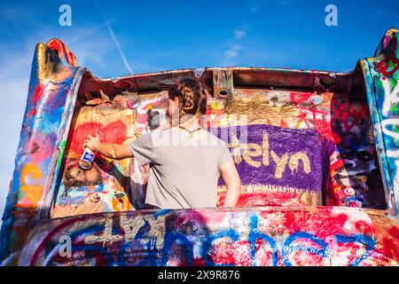 Girl Spray Painting Car auf der Cadillac Ranch, der öffentlichen Kunstinstallation und Skulptur in Amarillo, Texas, USA. Es wurde 1974 von Chip Lord, HUD, geschaffen Stockfoto