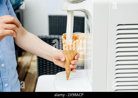 Nahaufnahme der Kinderhand mit der Eismaschine für den Heimgebrauch. Eiscreme für Softeis zubereiten und im Garten im Freien den Eiskegel eingießen. Stockfoto