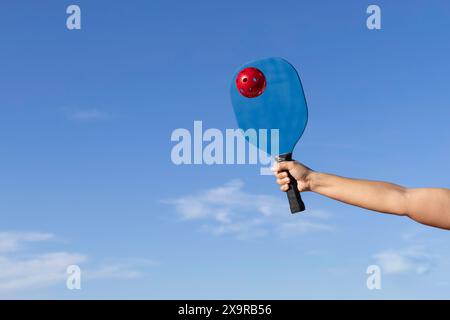 Pickleball-Spieler schlägt mitten im Spiel den roten Ball, mit dem Himmel im Hintergrund Stockfoto