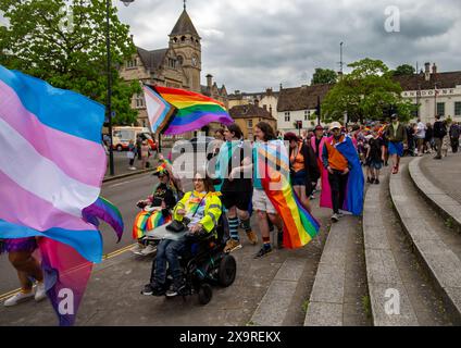 Menschen, die an einem bewölkten Tag am 1. Juni 2024 in Calne Wiltshire mit Regenbogenflaggen und farbenfrohen Outfits teilnehmen Stockfoto