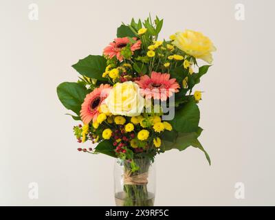 Ein Blumenstrauß mit lebhaften Farben und verschiedenen Arten. Der Blumenstrauß umfasst rosa Gerberas mit dunklen Zentren, gelbe Rosen und kleinere gelbe Strömungen Stockfoto