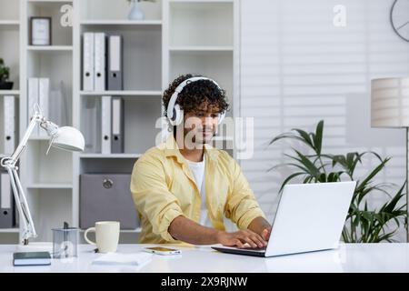 Junge Berufstätige, die von zu Hause aus arbeiten, Kopfhörer tragen und einen Laptop in einem modernen Büro benutzen. Fernarbeit und Produktivitätskonzept. Stockfoto