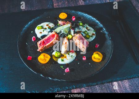 Thunfischsteak mit weißer Sauce, Gemüse und Spaghetti auf einem schwarzen Teller. Das Restaurant serviert Gerichte und mediterrane Küche. Hochwertige Fotos Stockfoto