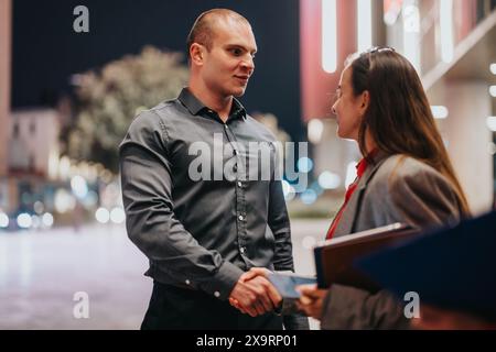 Junge Geschäftspartner begrüßen sich nachts mit Handschlag Stockfoto