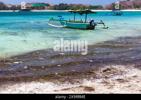 Boot neben schwimmendem Kunststoff und Müll in einem warmen, tropischen Ozean in Tanjung aan, Lombok, Indonesien Stockfoto