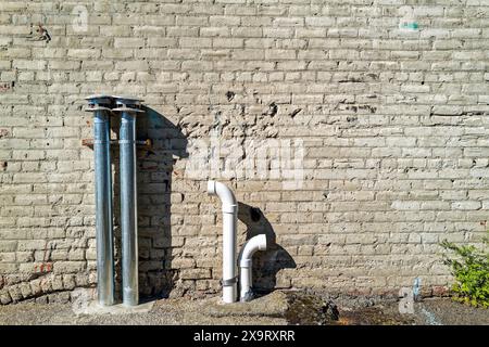 Aluminium- und PVC-Lüftungsrohre sind im Boden neben der äußeren Ziegelwand eines Gebäudes installiert Stockfoto