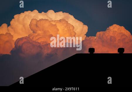 Ein Hausdach ist nach einem intensiven Sommergewitter vor bunten Cumulonimbus-Wolken geschildert. Stockfoto