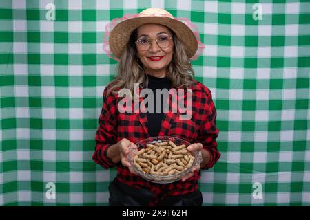 Frau in typischer Kleidung, die einen Strohhut trägt und ein Glastablett mit Erdnüssen darin hält. Essen vom Sao Joao Festival. Isoliert auf grünem und weißem CH Stockfoto