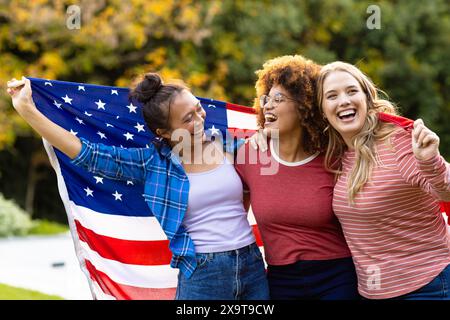 Glückliche, vielfältige Freundinnen, bedeckt mit der Flagge der usa im Garten Stockfoto