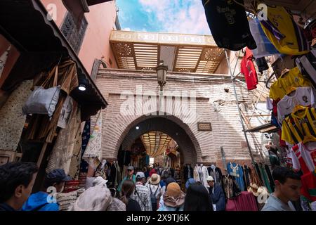 Jemaa el-Fnaa, Marrakesch, Marokko - 18. März 2024: Unter klarem Himmel nähert sich eine energiegeladene Menschenmenge dem bogenförmigen Markteingang. Lokale Waren auf dem Wareneingang Stockfoto