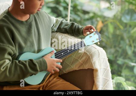 Zugeschnittenes Bild eines Jungen, der vor dem Spielen Ukulele abstimmt Stockfoto