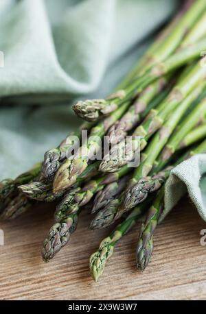 Ein Haufen frisch geernteter Spargelspeere ist ordentlich auf einem rustikalen Holztisch angeordnet, deren Grün- und Violettöne dezent durch die sanfte Note hervorgehoben werden Stockfoto