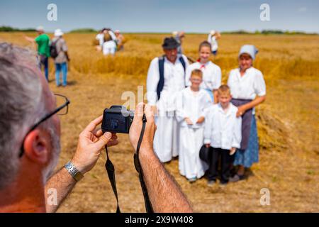 Der Fotograf hält eine Fotokamera, er macht Fotos, betrachtet die Kamera der Familie in weißen Volkstrachten, wie sie im Weizenfeld steht und posiert Stockfoto