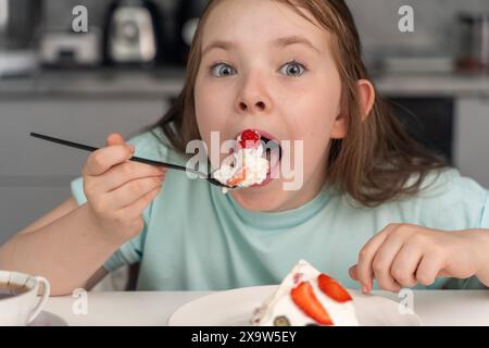 Das fröhliche kleine Mädchen isst Kuchen und steckt ihr ein großes Stück Dessert in den Mund. Ausgewählter Fokus. Hochwertige Fotos Stockfoto