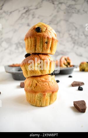 Ein Stapel köstlicher Heidelbeermuffins und Heidelbeeren auf einem weißen Tisch. Gebackene Beeren und Schokolade auf dem Brett. Blaubeermuffins. Stockfoto