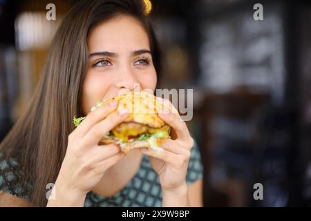 Glückliche Frau, die in einem Restaurant einen Hamburger isst und wegblickt Stockfoto