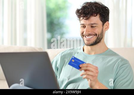 Glücklicher Mann, der zu Hause online mit Laptop und Kreditkarte kauft Stockfoto