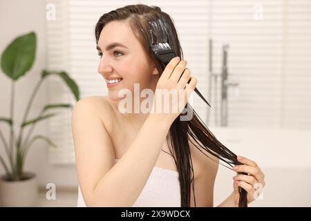 Junge Frau, die Haarmaske im Badezimmer aufträgt Stockfoto
