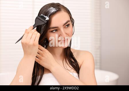Junge Frau, die Haarmaske im Badezimmer aufträgt Stockfoto