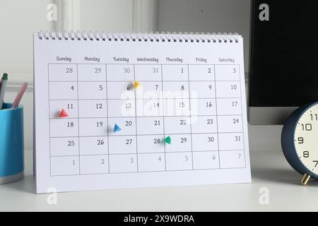 Zeitplan. Kalender mit gekennzeichneten Daten, Wecker und Schreibwaren auf weißem Tisch drinnen Stockfoto