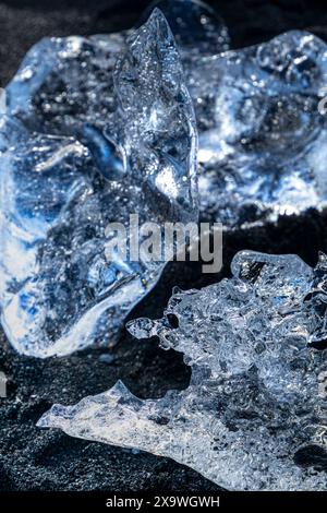 Ein Stück Eis liegt auf dem schwarzen Sand des Diamantstrandes. Das Licht erzeugt hypnotische Reflexionen durch das Eis Stockfoto