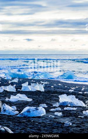 Eine Person steht an einem Strand mit viel Eis. Das Eis ist am ganzen Strand verstreut und die Person blickt auf das Meer Stockfoto