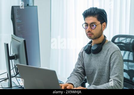 Der Prompt-Ingenieur des asiatischen Mannes entwickelt eine Codierungs-App mit Softwaredaten, die vor dem Computermonitor im Büro sitzen Stockfoto