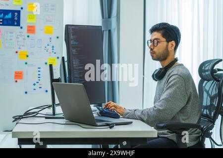 Der Prompt-Ingenieur des asiatischen Mannes entwickelt eine Codierungs-App mit Softwaredaten, die vor dem Computermonitor im Büro sitzen Stockfoto