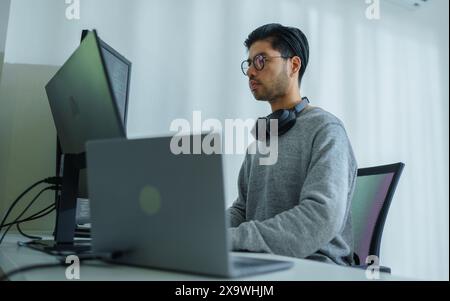 Der Prompt-Ingenieur des asiatischen Mannes entwickelt eine Codierungs-App mit Softwaredaten, die vor dem Computermonitor im Büro sitzen Stockfoto