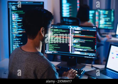 Asiatische Softwareentwickler arbeiten auf mehreren Bildschirmen und zeigen nachts in modernen Büros Code- und Anwendungsdiagramme an Stockfoto