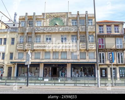 PORTO, PORTUGAL - 24. APRIL 2024: Art déco-Gebäude des Textilgeschäfts Armazens Cunhas mit farbenfrohem Pfau und dem Motto „Wir verkaufen billiger“ auf der Fassade in Por Stockfoto