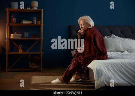 Ältere Frau im Pyjama, die auf dem Bett sitzt und Einsamkeit spürt Stockfoto
