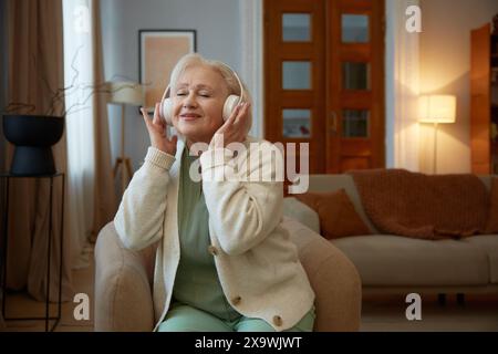 Grauhaarige ältere Frau im Kopfhörer, die Musik hört Stockfoto