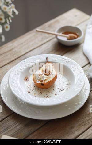 Birne mit Honig gebacken mit Eis, Walnüssen, Zimt, Gewürzen mit Sauce auf weißem Teller auf Holztisch. Stockfoto