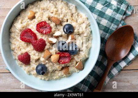 Haferbrei mit Himbeeren, Heidelbeeren und Mandeln in einer Schüssel auf Holztisch Stockfoto