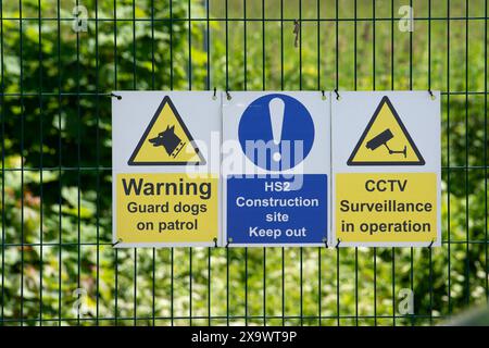 Wendover, Großbritannien. Juni 2024. Ein Schild, das die Menschen warnt, dass HS2 Wachhunde auf der Baustelle hat und CCTV-Überwachung durchführt. HS2 führt die Bauarbeiten in Wendover an der neuen Hochgeschwindigkeitsbahnverbindung von London nach Birmingham fort. Zwei riesige Y-förmige Viaduktpiers wurden nun gebaut, die den HS2 Small Dean Viaduct unterstützen werden, der ironischerweise die bestehende Chilterns Railway-Strecke überqueren wird, die bereits Passagiere nach Birmingham befördert. HS2 wird auch Small Dean Lane und die A413 unter dem Viadukt neu ausrichten. Ein Großteil des ehemaligen Ackerlandes und der Landschaft am Stadtrand von Wendover ist heute u Stockfoto