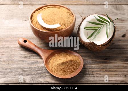 Kokosnusszucker in Schüssel, Löffel, Obst und Palmblätter auf Holztisch, Nahaufnahme Stockfoto