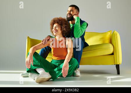 Glückliche afroamerikanische Freunde in lebendiger Kleidung sitzen auf einer gelben Couch und zeigen eine starke Verbundenheit und Verbundenheit. Stockfoto