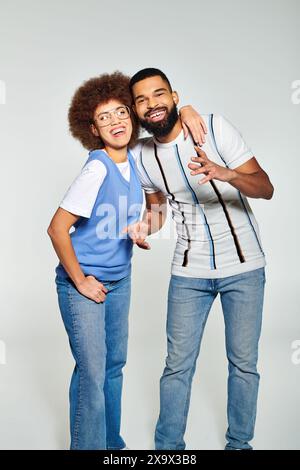 Ein afroamerikanischer Mann und eine afroamerikanische Frau in stilvoller Kleidung posieren für ein Bild mit grauem Hintergrund, das ihre Freundschaft zum Ausdruck bringt. Stockfoto