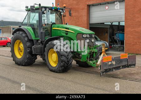 Der grüne schwarze Farmtraktor steht draußen auf der Straße neben einer Fabrikhalle Stockfoto