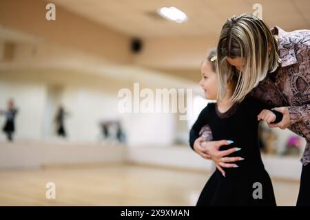 Ein junges Mädchen in einem Ballettkurs, das von ihrem Lehrer geführt wird, um Tanzbewegungen zu lernen. Die Szene fängt einen Moment des Lehrens und Lernens in einer Tanzszene ein Stockfoto