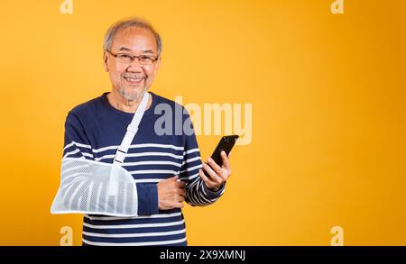Porträt asiatischer alter Mann warf seinen Arm und hielt das Handy-Studio isoliert gelben Hintergrund Stockfoto