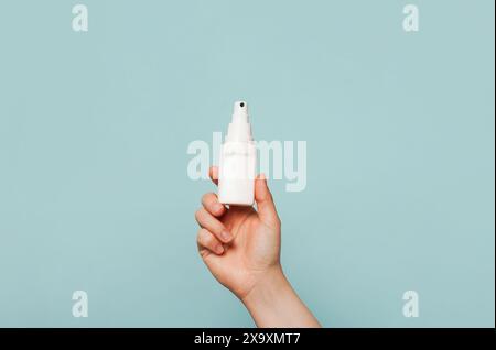 Eine Hand, die eine weiße Sprühflasche vor einem hellblauen Hintergrund hält Stockfoto