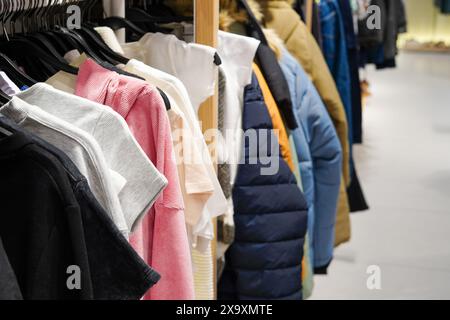 Ein Kleiderständer mit verschiedenen Kleidungsstücken, darunter T-Shirts, Jacken und Pullover in verschiedenen Farben und Materialien Stockfoto