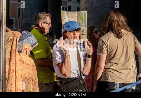 Während sie in der sengenden Hitze im Zentrum von Rom anstehen, werden zwei Damen kreativ, wie sie sich mit einer Karte von Rom und einem Fan unterbringen. Stockfoto