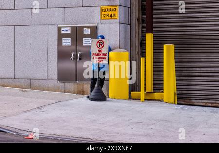 Ein Mann in blau gekleidet versteckt sich hinter einem Parkverbot, umgeben von leuchtend gelben Pollern in New York. Stockfoto