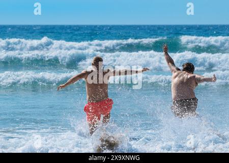 Zwei männliche Urlauber laufen in Fistral in Newquay in Cornwall in Großbritannien ins Meer. Stockfoto