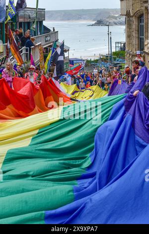 Das farbenfrohe Cornwall ist stolz auf das Banner der Pride-Flagge, das von den Teilnehmern der Parade im Zentrum von Newquay in Großbritannien gehalten wird. Stockfoto