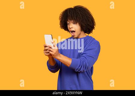 Junger Mann mit lockigem Haar reagiert auf Smartphone im Studio Stockfoto