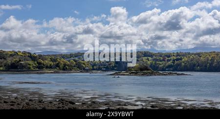 Die Leute fahren Kajakfahren auf der Menai-Straße mit der Menai-Hängebrücke und den Bergen von Snowdonia im Hintergrund. Anglesey, Nordwales. Stockfoto